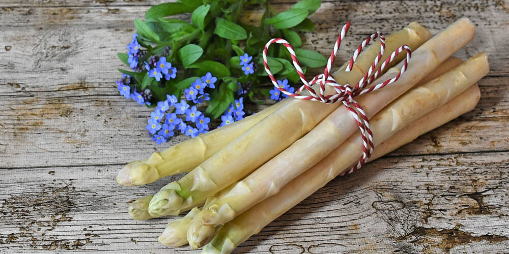 Ein frisches Bund weißer Spargel liegt auf einem rustikalen Holztisch