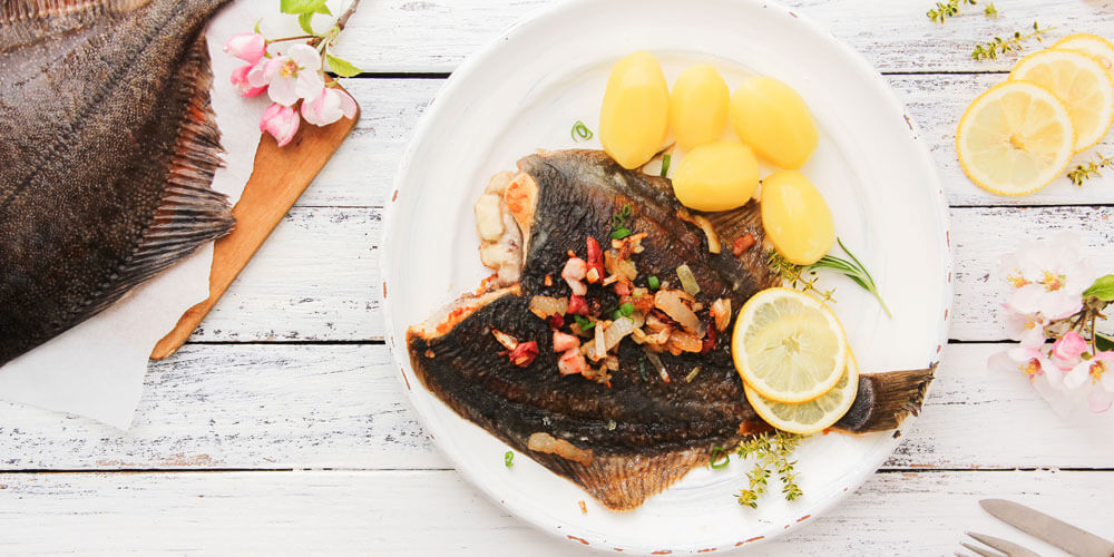 Maischolle, klassisch angerichtet auf einem Teller mit Salzkartoffeln, Zitronenscheibe und Gewürzen