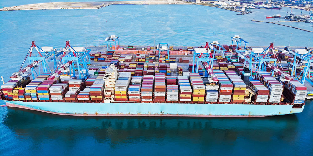 Großes voll beladenes Containerschiff läuft in einen Hafen ein.