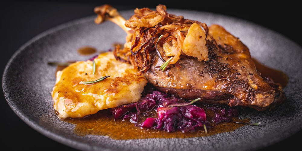 Gänsekeule mit Rotkohl und Beilagen festlich angerichtet auf einem Teller