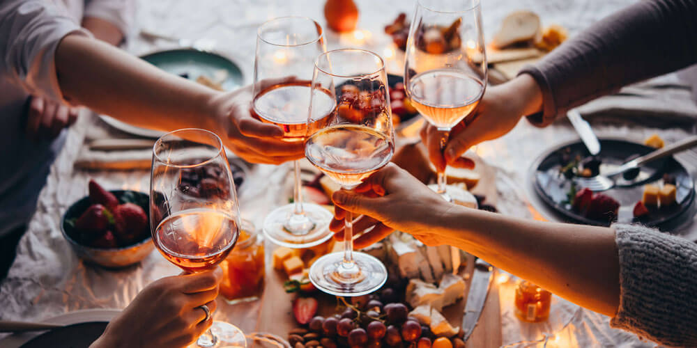 Mehrere Personen prosten sich am gedeckten Tisch mit Roséwein zu